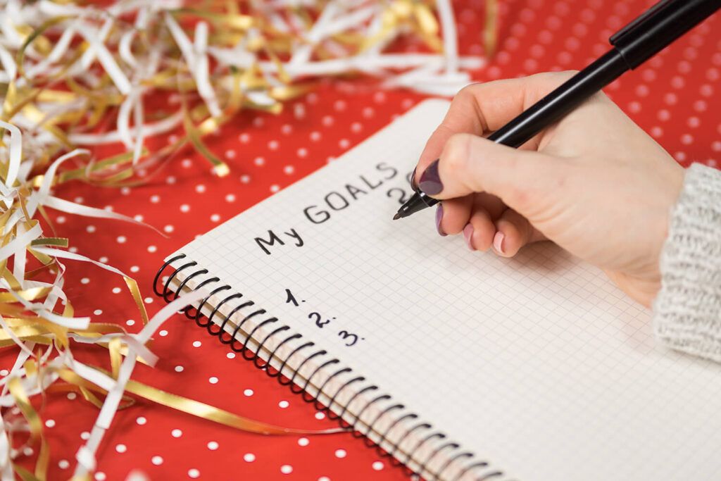 manos femeninas escribiendo mis objetivos 2020 cuaderno fondo rojo oropel concepto ano nuevo
